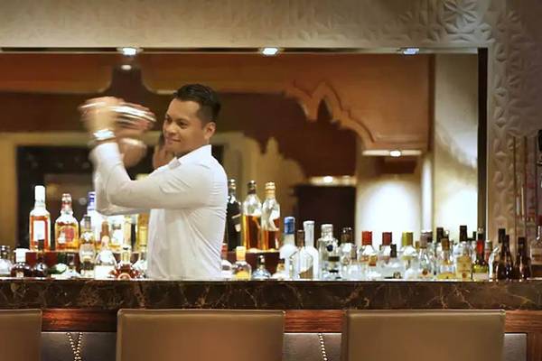 Cocktailbar im Hilton Ras Al Khaimah Beach Resort mit einem Barkeeper, der einen Cocktail mixt.