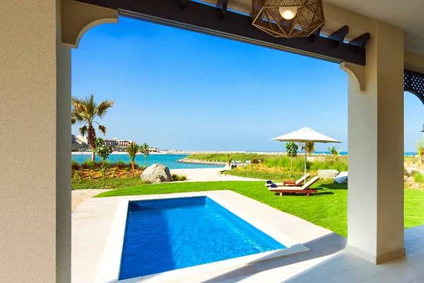 Außenansicht des Hilton Ras Al Khaimah Beach Resorts mit Pool, Loungebereich und Meerblick.