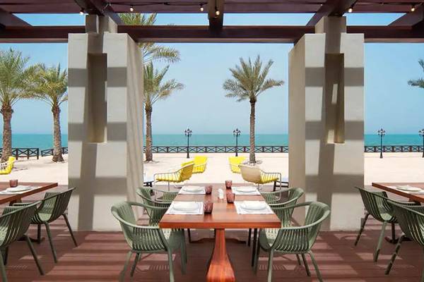 Außenbereich des Hilton Ras Al Khaimah Beach Resort mit Tischen, Stühlen und Blick auf den Strand und das Meer.