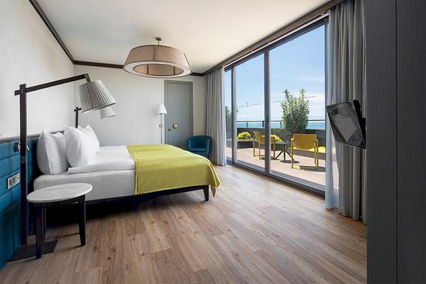 Innenansicht eines Zimmers im Voyage Belek Golf & Spa Hotel mit einem Bett, einem Tisch, Stühlen und einer Aussicht auf die Terrasse.