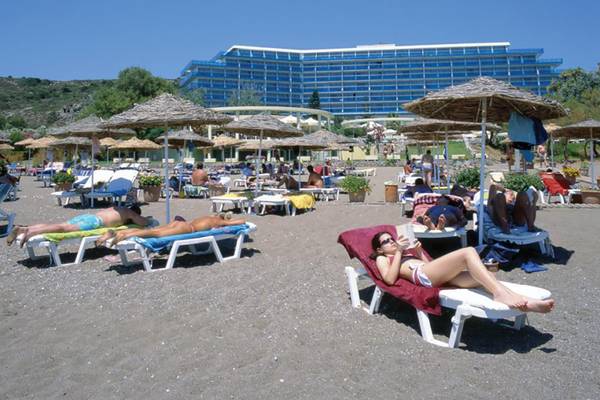 Gäste entspannen auf Liegestühlen am Strand vor dem Calypso Beach Hotel.