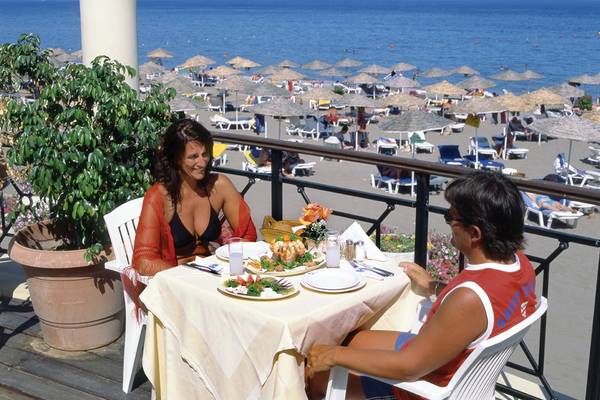 Zwei Gäste sitzen an einem Tisch auf der Terrasse des Calypso Beach Hotels mit Blick auf den Strand.