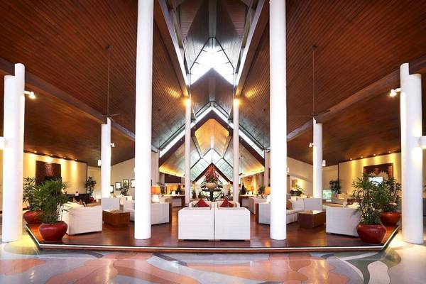 Lobby des Le Meridien Phuket Beach Resorts mit weißen Möbeln, hohen Säulen und braunen Holzdecken.