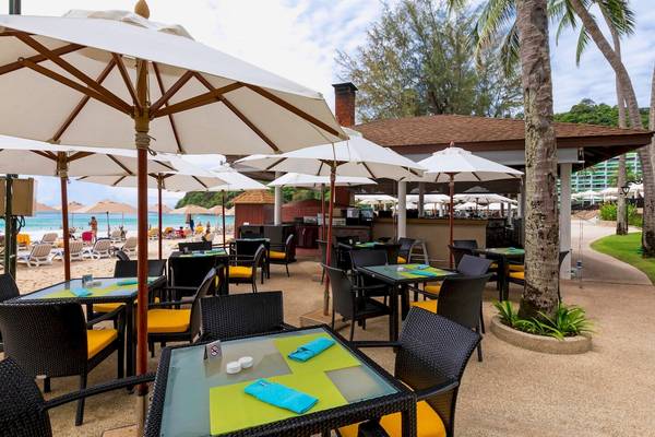 Restaurant am Strand des Le Meridien Phuket Beach Resorts mit Tischen und Stühlen unter großen Schirmen.