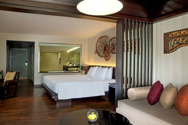 Schlafzimmer des Le Meridien Phuket Beach Resort mit Doppelbett, Sofa und Dekorelementen.