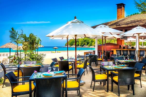 Terrasse des Le Meridien Phuket Beach Resorts mit Tischen und Stühlen unter weißen Sonnenschirmen am Strand
