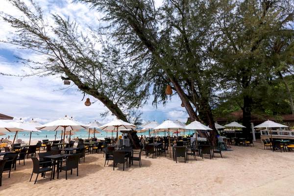 Restaurant im Freien am Strand des Le Meridien Phuket Beach Resorts mit Tischen und Stühlen unter Schirmen.
