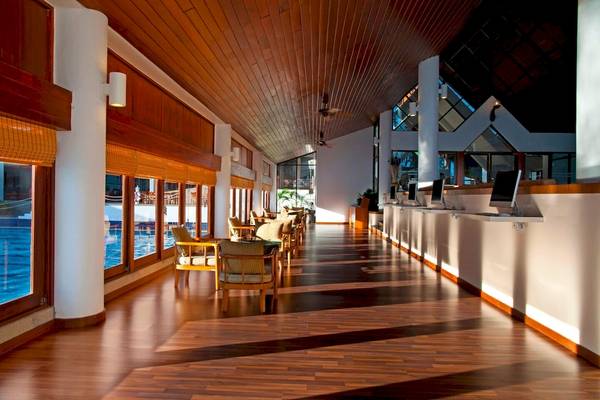 Innenbereich des Le Meridien Phuket Beach Resorts mit Holzboden, Sitzgruppen und Empfangstresen.