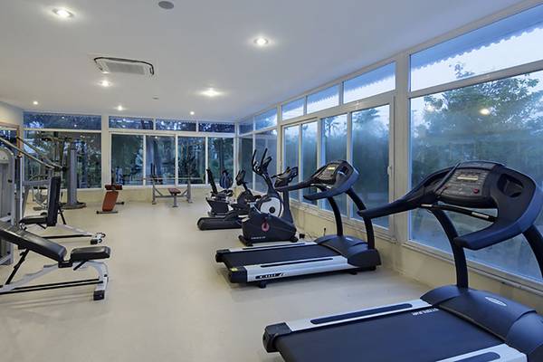 Fitnesscenter im Asteria Family Resort Side mit verschiedenen Geräten und großen Fenstern.