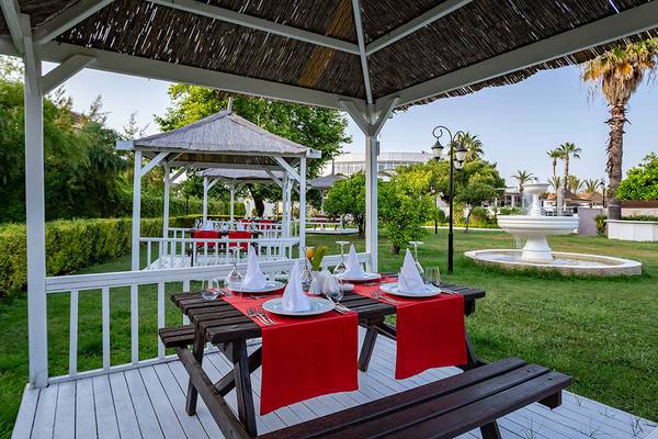 Gartensitzbereich im Asteria Family Resort Side mit roter Tischdecke und gedecktem Tisch.