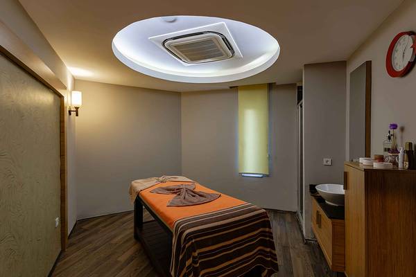 Massageraum im Asteria Family Resort Side mit einem Behandlungstisch, einer Lampe und einer Uhr.