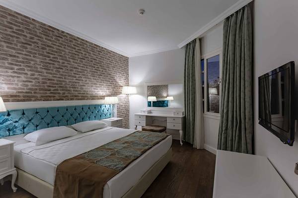 Hotelzimmer im Asteria Family Resort in Side mit einem Bett, Nachttischen, Lampen und einem Fernseher.