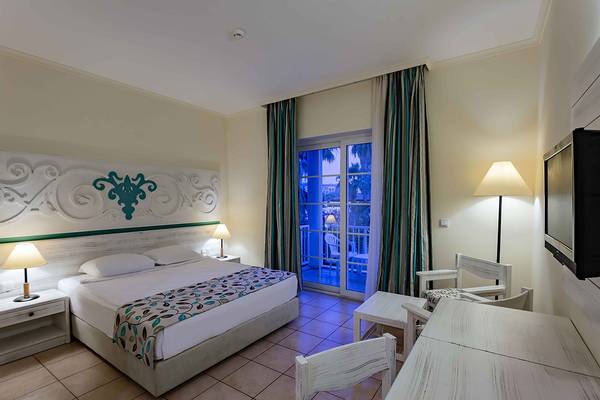 Innenansicht eines Hotelzimmers im Asteria Family Resort Side mit einem Bett, Nachttischen, Lampen und einem Fernseher.