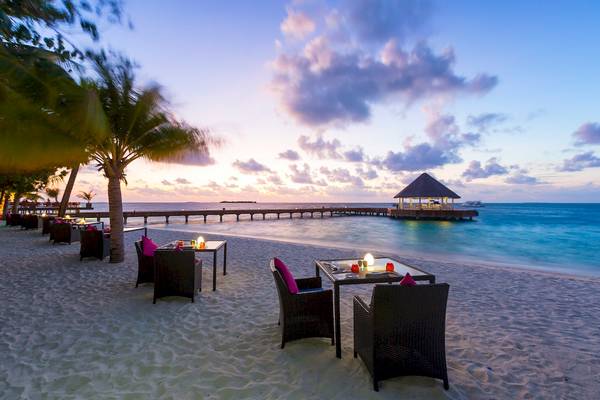 Sonnenuntergang am Strand des Sun Siyam Vilu Reef mit Pavillon und Tischen im Freien.