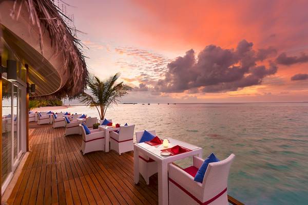 Außenterrasse des Sun Siyam Vilu Reef Hotels mit Tischen und Stühlen, die auf den Ozean hinausblicken, bei Sonnenuntergang