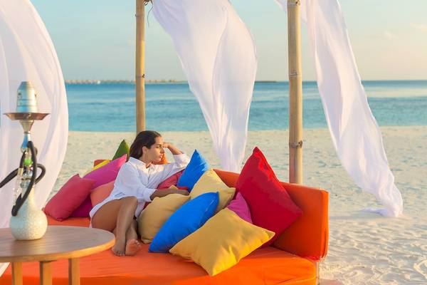 Frau auf orangem Sofa am Strand im Sun Siyam Vilu Reef Hotel