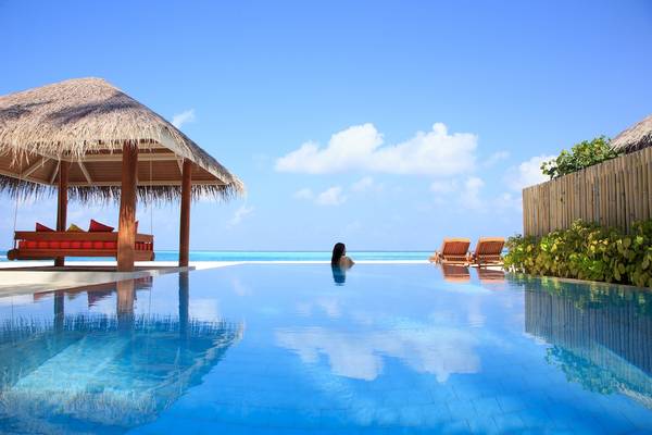 Ein Swimmingpool des Sun Siyam Vilu Reef Hotels mit einer Sonnenliege unter einem strohgedeckten Pavillon.
