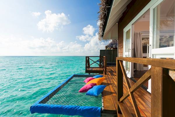 Terrasse des Sun Siyam Vilu Reef Hotels mit einem Netzbett und Kissen, am Wasserrand.