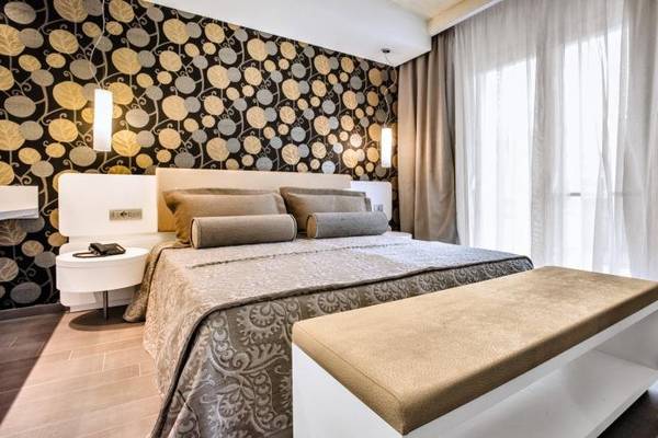 Schlafzimmer im Grand Hotel Resort Ma&Ma mit gemusterter Wand, Bett, Nachttisch und Bank
