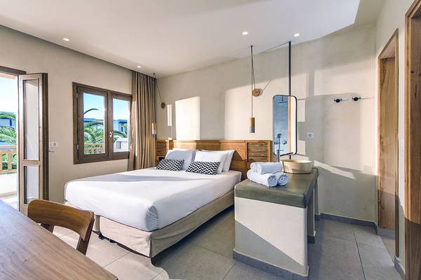 Innenansicht eines Schlafzimmers im Stella Village Hotel & Bungalows mit einem Bett, Fenstern und einem Balkon.