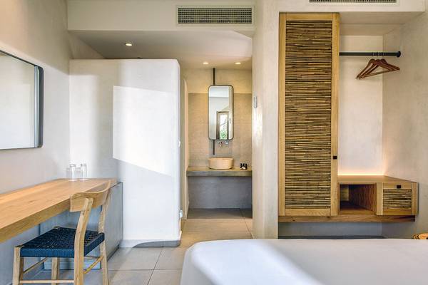 Innenansicht eines Zimmers im Stella Village Hotel & Bungalows mit Schreibtisch, Stuhl, Bett, Badezimmer und Spiegel.