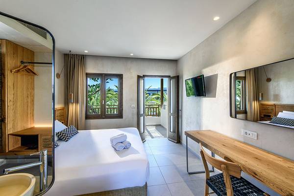 Ein modernes Schlafzimmer im Stella Village Hotel & Bungalows mit Doppelbett, offenem Balkon und Badezimmerspiegel.