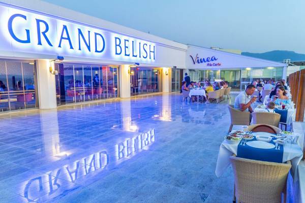 Außenbereich des Grand Belish Resort Hotel & Spa mit beleuchtetem Boden und Gästen an Tischen.