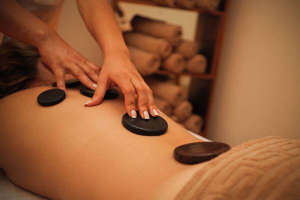 Massagebehandlung im Grand Belish Resort Hotel & Spa mit schwarzen Steinen auf dem Rücken einer Person.