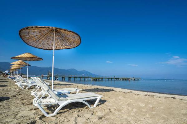 Strand mit weißen Sonnenliegen und Sonnenschirmen, Blick aufs Meer und eine Pier