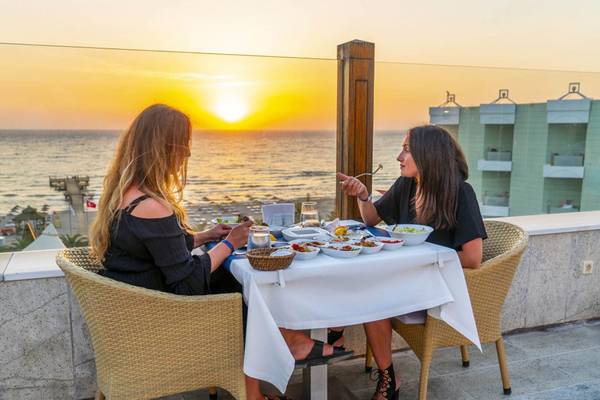 Zwei Frauen essen auf einem Balkon mit Meerblick während des Sonnenuntergangs.