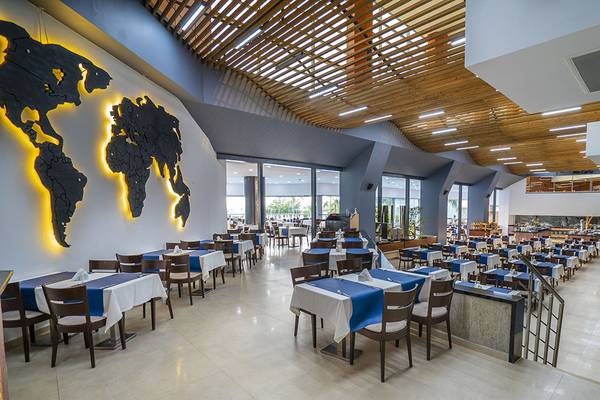 Innenraum des Grand Belish Resort Hotel & Spa mit einer Weltkarte an der Wand und vielen blau-weiß gedeckten Tischen.