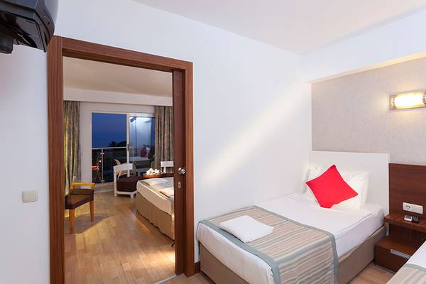 Innenansicht eines Schlafzimmers im Seher Resort & Spa Hotel mit zwei Betten, Nachttischen und einem Balkon.