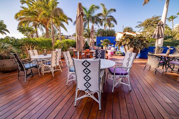 Außenterrasse des Bohemia Suites & Spa Hotels mit blauen Wänden, Holzboden und runden Tischen.