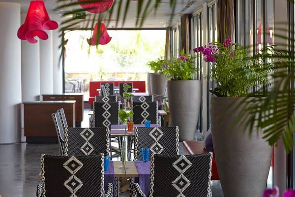 Boho-Suites-und-Spa-Hotelspeisebereich mit Tisch und Sesseln, großen Pflanzen und rotem Baldachin.