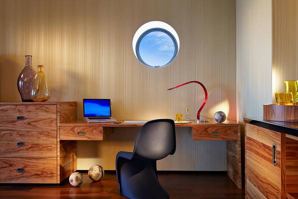 Ein hölzerner Schreibtisch mit Laptop, Lampe und rundem Fenster im Hintergrund.