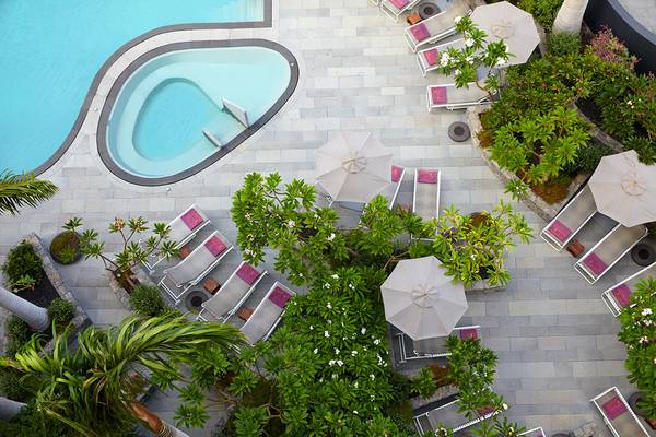 Herzförmiger Pool mit Liegen und Sonnenschirmen auf dem Hotelgelände.