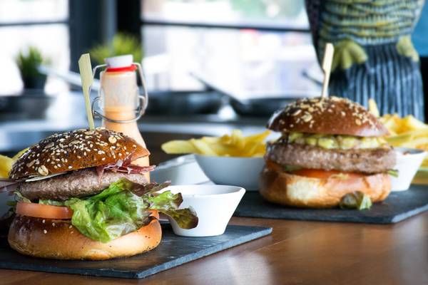 Zwei Burger auf einem Tisch mit Pommes und Saucen.