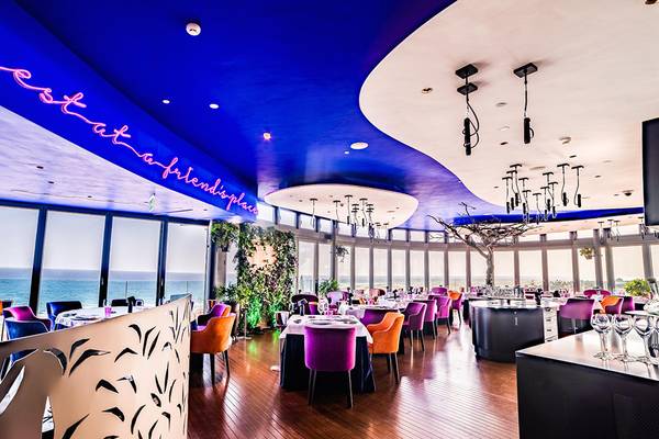 Innenansicht des Restaurants Bohemia Suites & Spa mit blauer Decke, neonfarbener Schrift und Blick auf den Ozean.