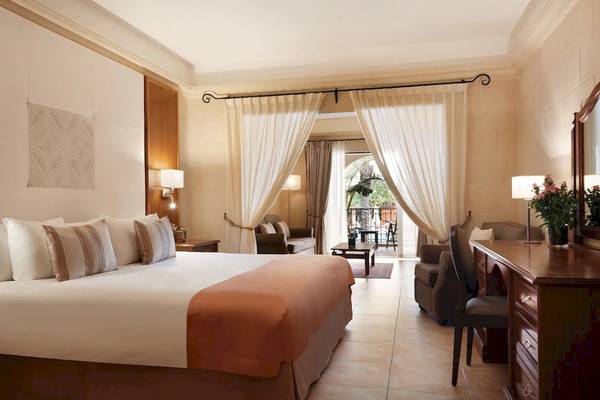 Innenansicht einer Suite im Kempinski Hotel San Lawrenz Malta mit Bett, Sofa, Schreibtisch und Balkon.