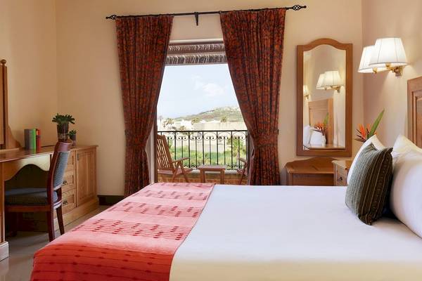 Hotelzimmer mit einem Bett, einem Balkon, Spiegeln und einem Schreibtisch im Kempinski Hotel San Lawrenz Malta.