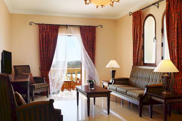 Wohnzimmer im Kempinski Hotel San Lawrenz Malta mit Couch, Tisch, Lampen und Fernseher.
