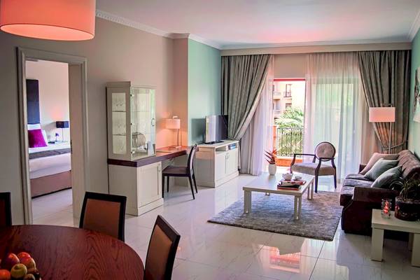Innenansicht einer Suite im Kempinski Hotel San Lawrenz Malta mit Wohnzimmer, Schlafzimmer und Balkon.