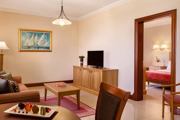 Innenansicht eines Hotelzimmers im Kempinski Hotel San Lawrenz, Malta, mit Couch, Fernseher, Tisch und Lampe.