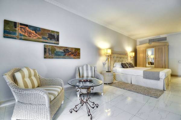 Zimmer im Kempinski Hotel San Lawrenz Malta mit Bett, Sesseln und Kunstwerken an der Wand.