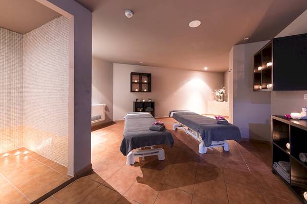 Massage-Bereich im AluaSoul Costa Adeje Hotel mit zwei Massagetischen und einem Regal mit Kerzen.