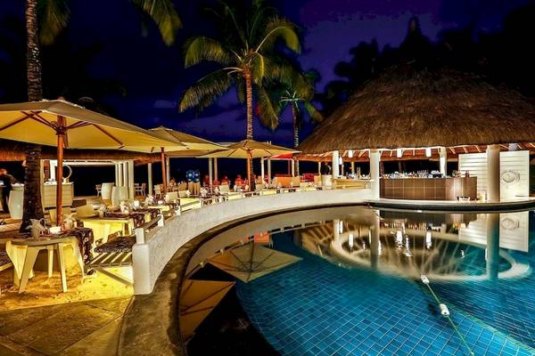 Außenpoolterrasse des Constance Belle Mare Plage Hotels bei Nacht mit Tischen und Stühlen unter Sonnenschirmen.