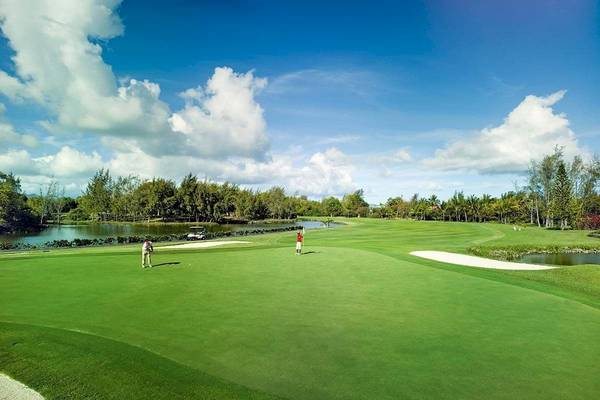 Golfplatz am Constance Belle Mare Plage Hotel mit zwei Spielern und einem See im Hintergrund.