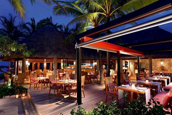 Abendansicht des Restaurants im Constance Belle Mare Plage Hotel mit holzigen Tischen und Stühlen im Freien.