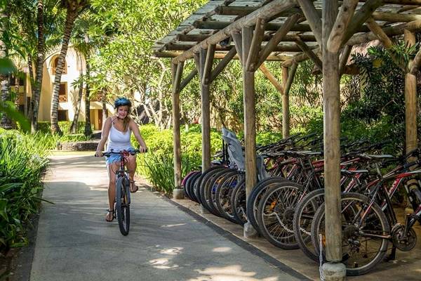 Eine Frau fährt auf einem Fahrrad am Constance Belle Mare Plage vorbei an vielen gemieteten Fahrrädern.