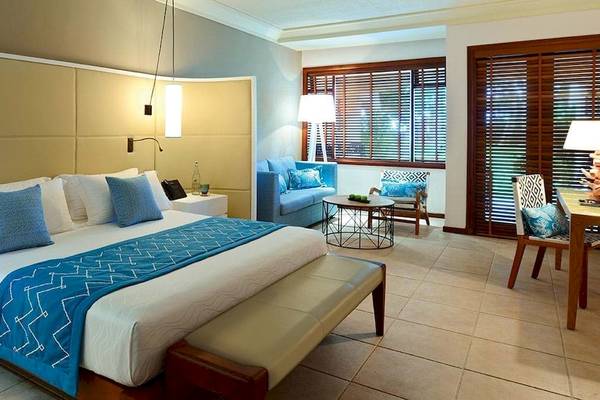 Schlafzimmer im Constance Belle Mare Plage Hotel mit Bett, Kissen, Nachttischen und Sitzbereich.